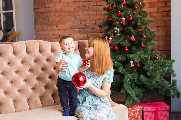 Portret van gelukkige moeder en de lachende kerstbal van de babyholding tegen binnenlands feestelijk binnenland met