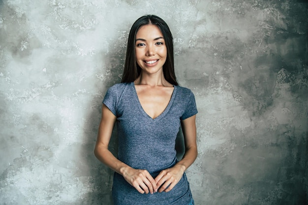 Portret van gelukkige mooie jonge Aziatische vrouw in t-shirt over betonnen muur