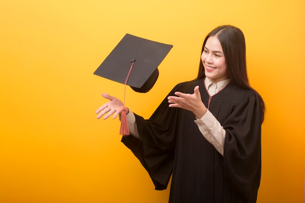 Portret van gelukkige mooie vrouw in graduatietoga op gele ruimte