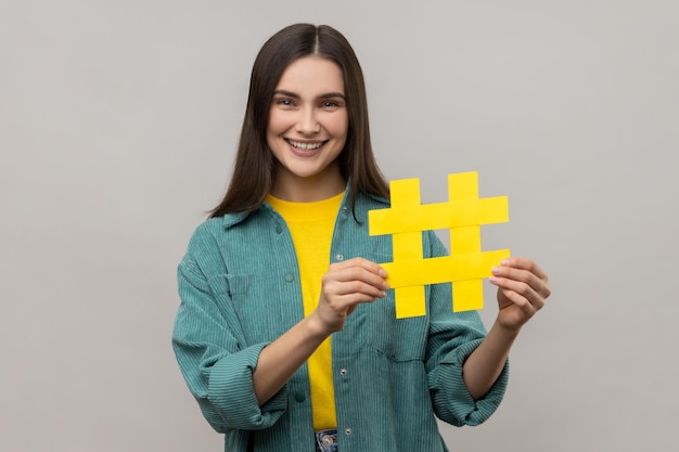 Portret van gelukkige mooie vrouw met hashtag symbool bevordering van virale onderwerp in sociaal netwerk tagging blog trends dragen casual stijl jas Indoor studio shot geïsoleerd op grijze achtergrond