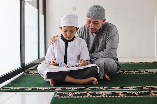 Portret van gelukkige moslimvader die zoon leert de koran te lezen en samen bidt in de moskee