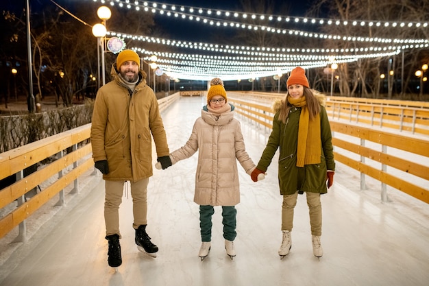 Portret van gelukkige ouders met dochter hand in hand terwijl ze samen schaatsen in het park