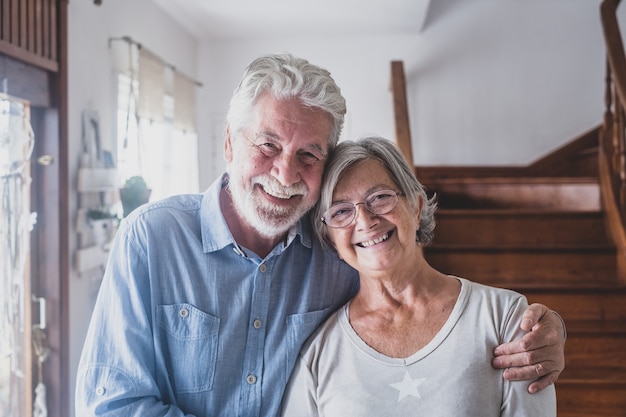 Portret van gelukkige paar oude mensen senioren knuffelen samen, kijken naar de camera, houden van volwassen vrouw en echtgenoot met een gezonde speelse glimlach die zich voordeed op familiefoto thuis.