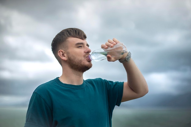 Portret van gelukkige positieve dorstige man jonge knappe man drinkt puur vers mineraalwater uit plastic fles op natuurlijke zee oceaan achtergrond in tropisch land met fles in de hand