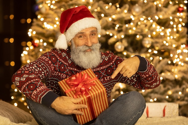 Portret van gelukkige Santa Claus-zitting bij zijn ruimte thuis dichtbij Kerstboom.