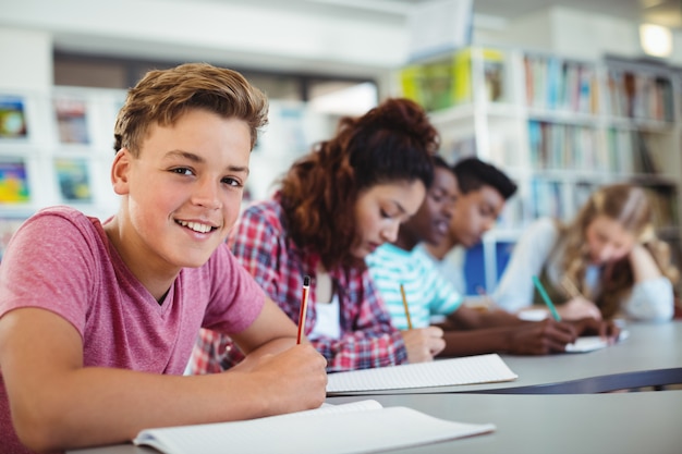 Portret van gelukkige schooljongen die in bibliotheek bestudeert