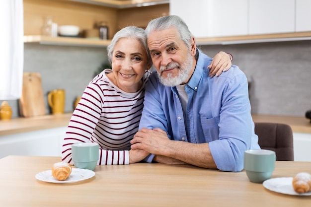 Portret van gelukkige senior echtgenoten poseren aan tafel in de keuken