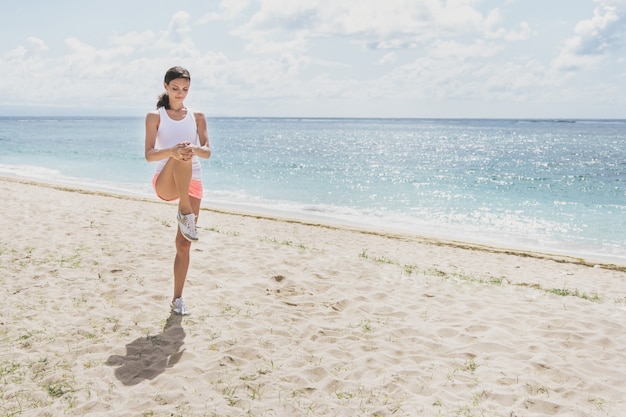 Portret van gelukkige sportieve vrouw doet benen die zich uitstrekt voordat joggen op het strand
