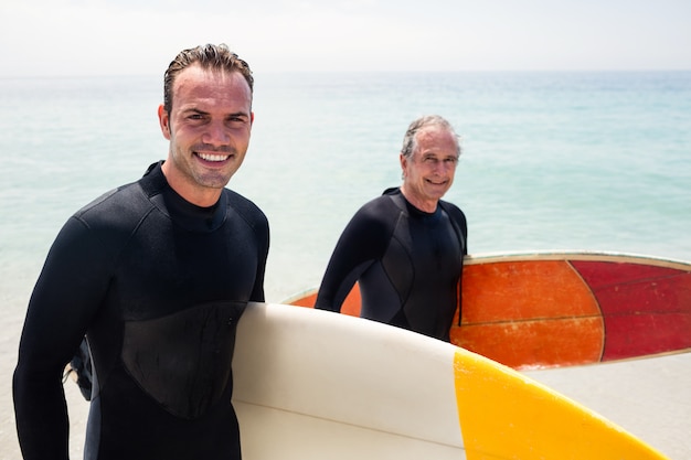 Portret van gelukkige vader en zoon in wetsuit die een surfplank houden