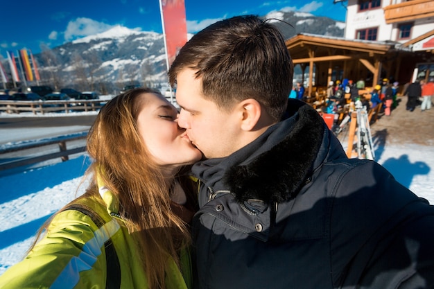 Portret van gelukkige verliefde paar zoenen op winterskiresort op zonnige dag