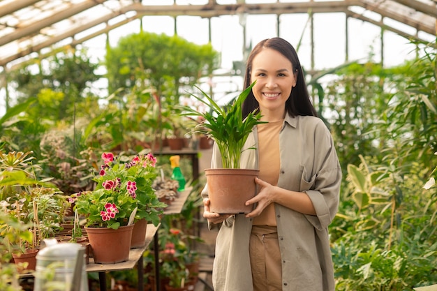 Portret van gelukkige vrij Aziatische vrouw met potplant in moderne broeikas