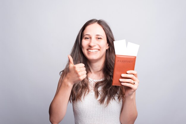 Portret van gelukkige vrouw die duim en paspoort met vliegtickets toont