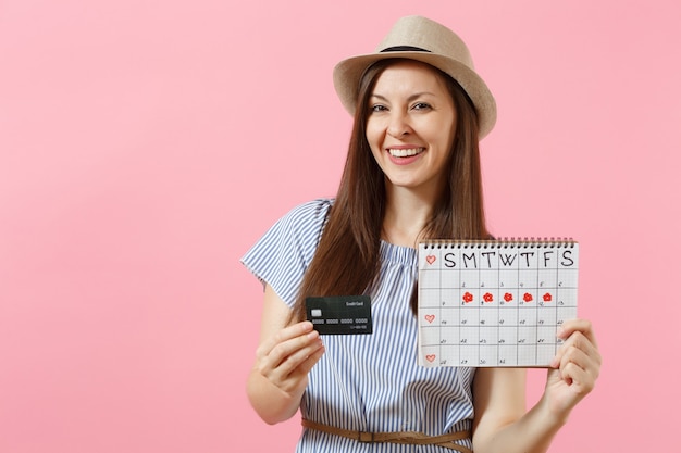 Portret van gelukkige vrouw in blauwe jurk, hoed met creditcard, menstruatiekalender, menstruatiedagen controleren geïsoleerd op trending roze achtergrond. Medische gezondheidszorg gynaecologische concept. Ruimte kopiëren.