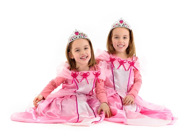 Foto portret van gelukkige zusters die een prinsesjurk dragen en tegen een witte achtergrond zitten