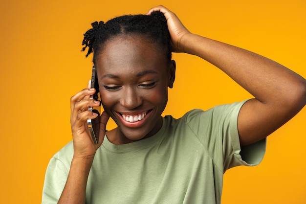 Portret van gelukkige zwarte vrouw praten op mobiele telefoon in gele studio