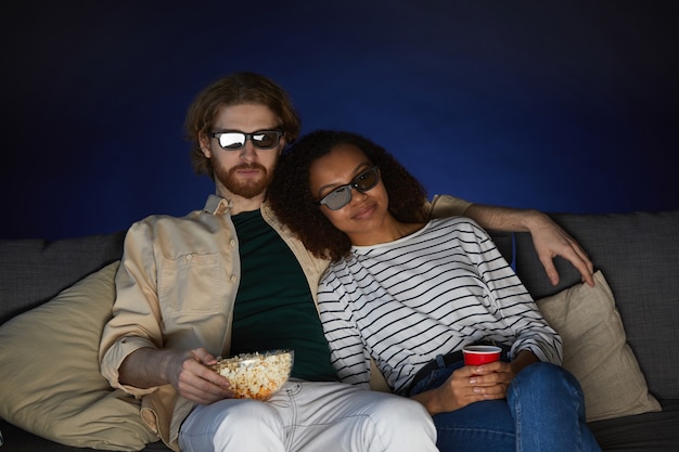 Portret van gemengd ras moderne paar kijken naar film en stereoglazen dragen zittend op de Bank in een donkere kamer