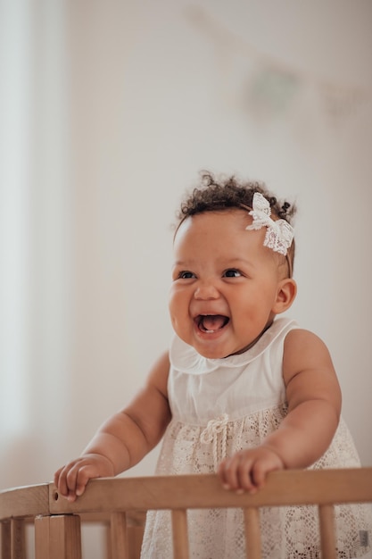 Portret van gemengd ras peutermeisje in ronde houten babywieg in gezellige kinderkamer neutrale tinten