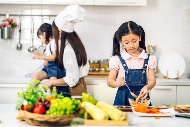 Foto portret van geniet van gelukkige liefde aziatische familie moeder en klein aziatisch meisje dochter kind plezier helpen bij het koken van voedsel gezond eten samen met verse groentesalade en sandwich ingrediënt in de keuken