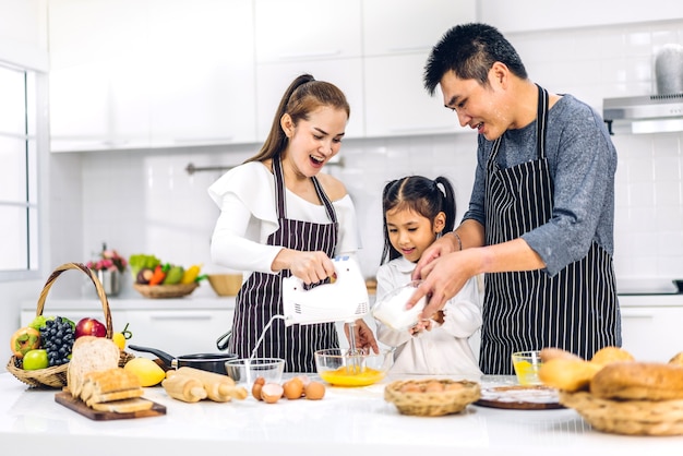 Portret van genieten van gelukkige liefde Aziatische familie vader en moeder met Aziatische meisje dochter kind plezier koken samen met koekjes bakken en cake ingrediënten op tafel in de keuken