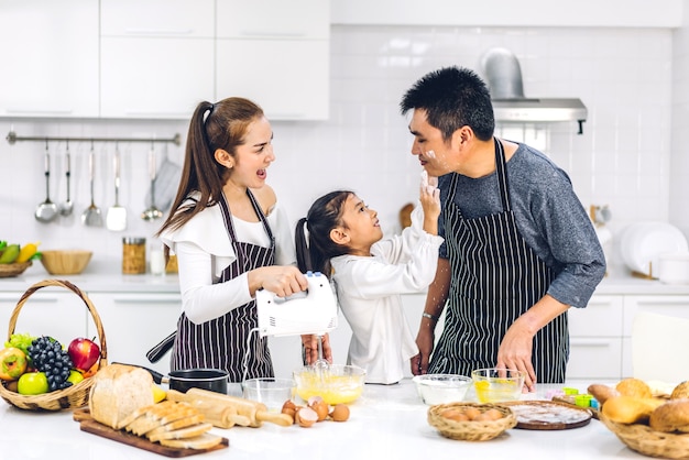 Portret van genieten van gelukkige liefde Aziatische familie vader en moeder met Aziatische meisje dochter kind plezier koken samen met koekjes bakken en cake ingrediënten op tafel in de keuken