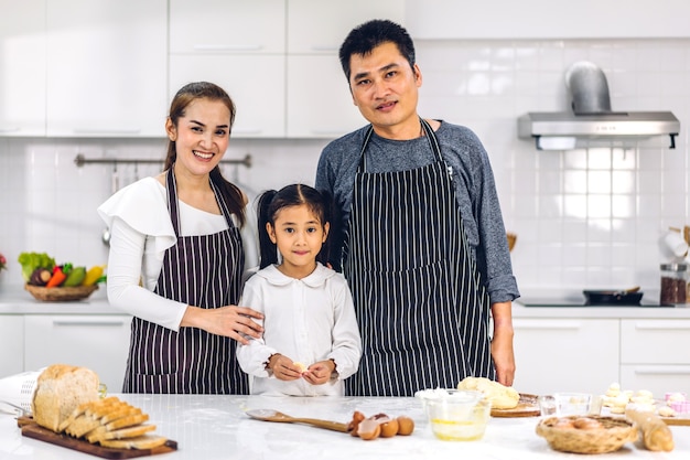 Portret van genieten van gelukkige liefde Aziatische familie vader en moeder met Aziatische meisje dochter kind plezier koken samen met koekjes bakken en cake ingrediënten op tafel in de keuken