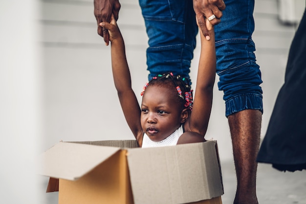Portret van genieten van gelukkige liefde zwarte familie afro-amerikaanse vader en klein afrikaans meisje, zittend in een kartonnen doos