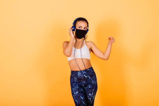 Portret van geschikte Afrikaanse vrouw die gezichtsmasker draagt. Sportieve vrouw in fitnesskleding staande op een gele achtergrond.