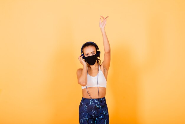 Portret van geschikte Afrikaanse vrouw die gezichtsmasker draagt. Sportieve vrouw in fitnesskleding staande op een gele achtergrond.