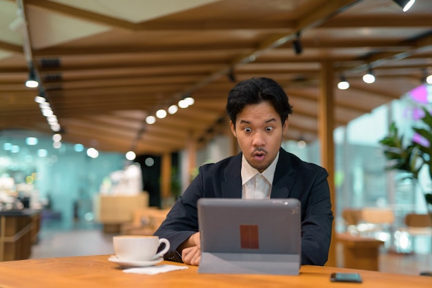 Portret van geschokte Aziatische zakenman in koffiewinkel die digitale tabletcomputer gebruikt