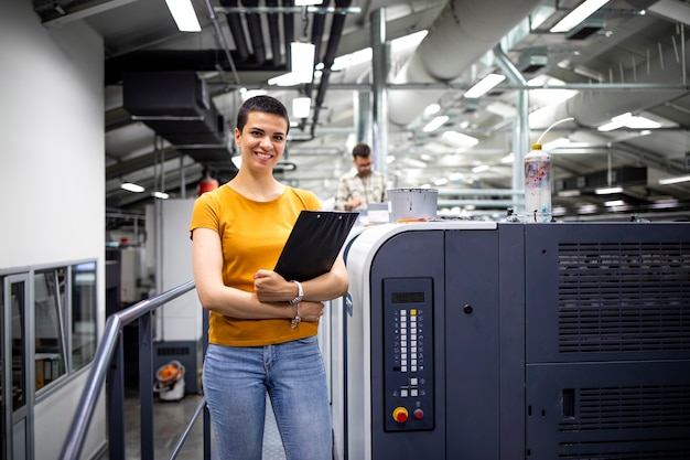 Portret van getalenteerde vrouwelijke ontwerper die bij de moderne drukmachine staat in de drukkerij.