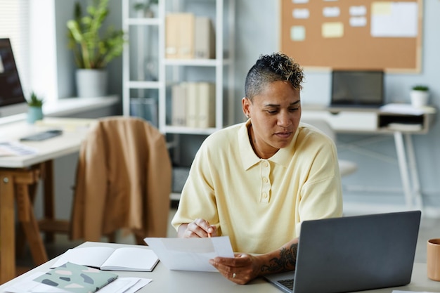 Portret van getatoeëerde Afro-Amerikaanse vrouw met behulp van laptop op kantoor werkplek en het dragen van casual clot