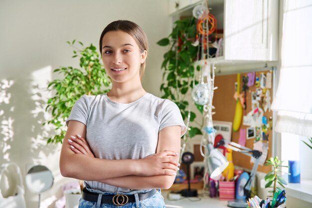 Portret van glimlachend tienermeisje 14 15 jaar oud kijkt naar de camera thuis in de kamer Mooie zelfverzekerde vrouwelijke student met gevouwen handen Adolescentie jeugd levensstijl studenten concept