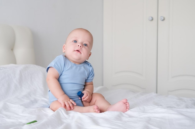 portret van glimlachende babyjongen met grote blauwe ogen in bodysuit op wit beddengoed Gezond pasgeboren kind