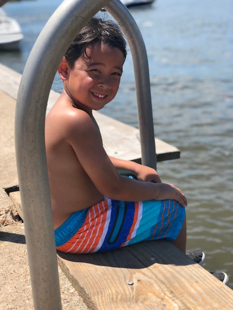 Portret van glimlachende hemdloze jongen die op de pier over het meer zit