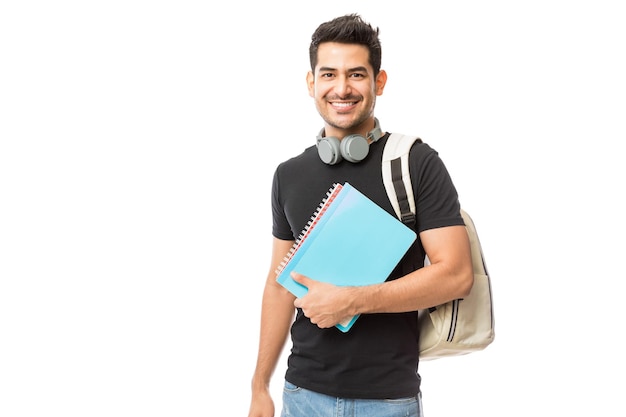 Portret van glimlachende jonge student met boeken en rugzak tegen witte achtergrond