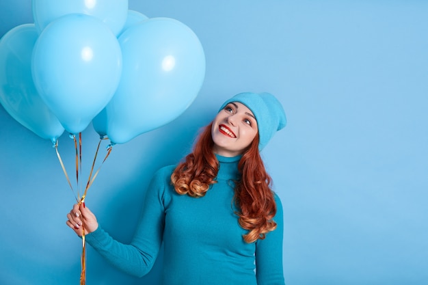 Portret van glimlachende jonge vrouw die in vrijetijdskleding opzij haar ballons bekijkt