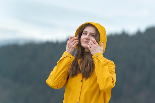 Portret van glimlachende jonge vrouw in gele regenjas buiten Bos op achtergrond Meisje op wandeling in de herfst camera kijken