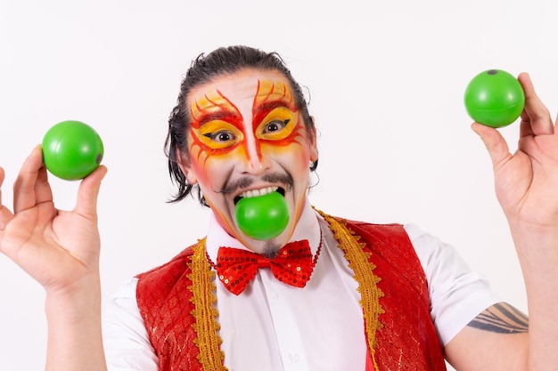 Portret van glimlachende jongleur die met groene ballen jongleert die op witte achtergrond worden geïsoleerd