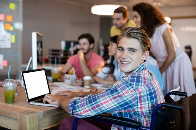 Portret van glimlachende man met behulp van laptop tijdens het werken met zijn team op kantoor