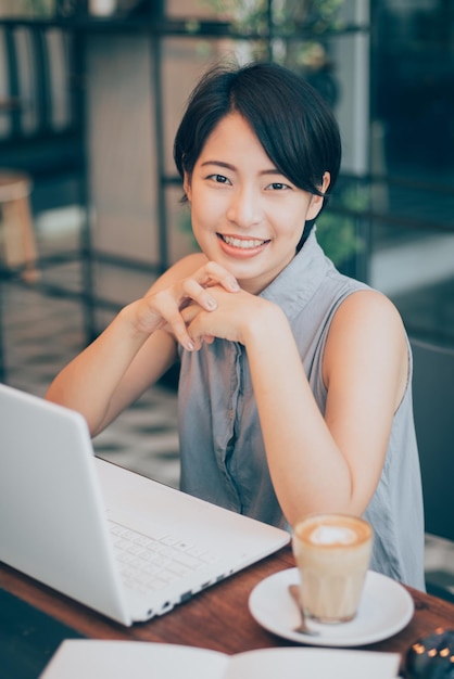 Portret van glimlachende mooie jonge vrouw met laptop en koffiekop op tafel