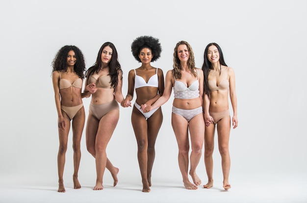 Portret van glimlachende multi-etnische vrouwen in lingerie die op een witte achtergrond lopen