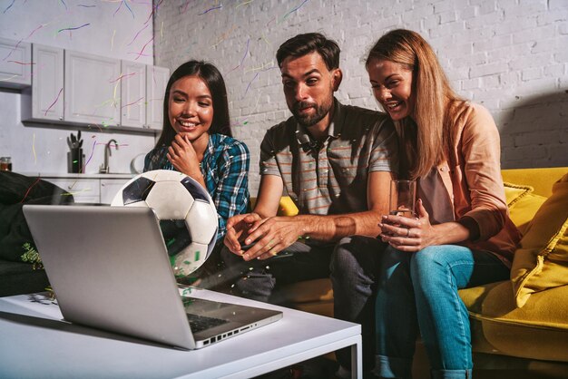 Foto portret van glimlachende vrienden die thuis een laptop gebruiken