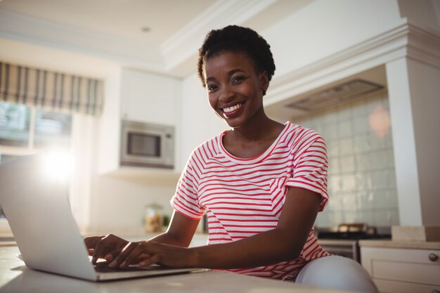 Portret van glimlachende vrouw die laptop in keuken met behulp van