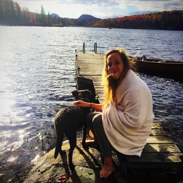 Foto portret van glimlachende vrouw met hond die op de pier over het meer zit
