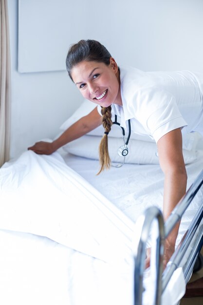 Portret van glimlachende vrouwelijke arts die het bed voorbereidt