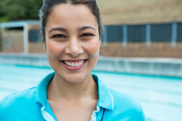 Portret van glimlachende vrouwelijke coach die zich dichtbij zwembad in het recreatiecentrum bevindt