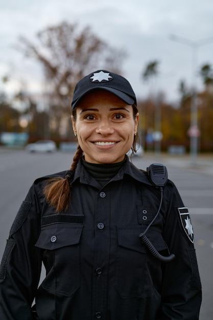 Portret van glimlachende vrouwelijke politieagent op straat die opzij kijkt. Geschoten met onscherpe achtergrond