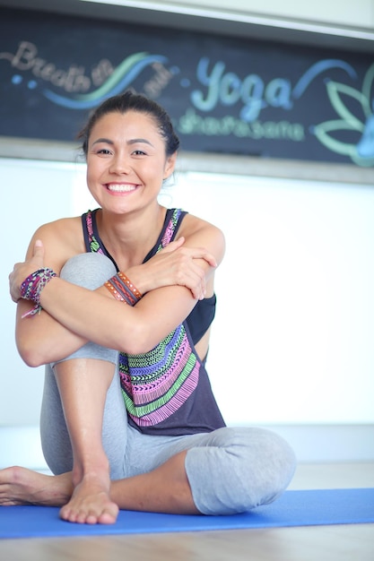 Portret van glimlachende yogavrouw die op yogamat zit na training bij yogastudio yogavrouw