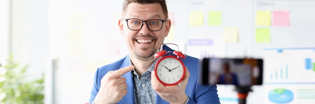 Portret van glimlachende zakenman die rode wekker in zijn handtijdbeheer houdt en