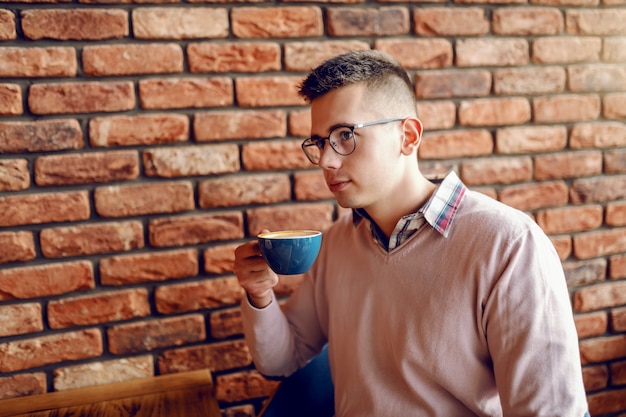 Portret van goed geklede jonge man zit in de cafetaria en koffie drinken